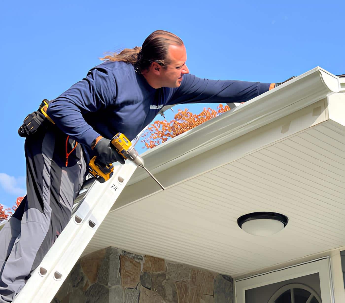 Professional contractor installing white aluminum gutters on a residential home with clear blue sky and autumn foliage